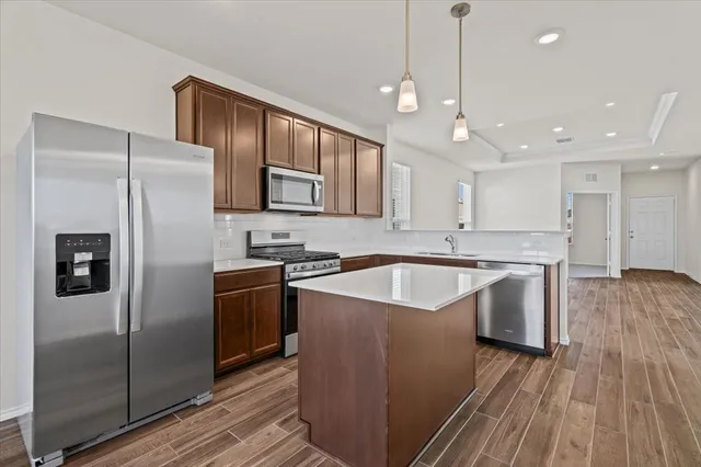 a kitchen with stainless steel appliances granite countertop a refrigerator a sink dishwasher a stove and white countertops with wooden floor