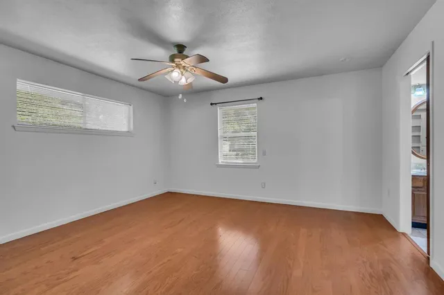 an empty room with wooden floor chandelier fan and windows