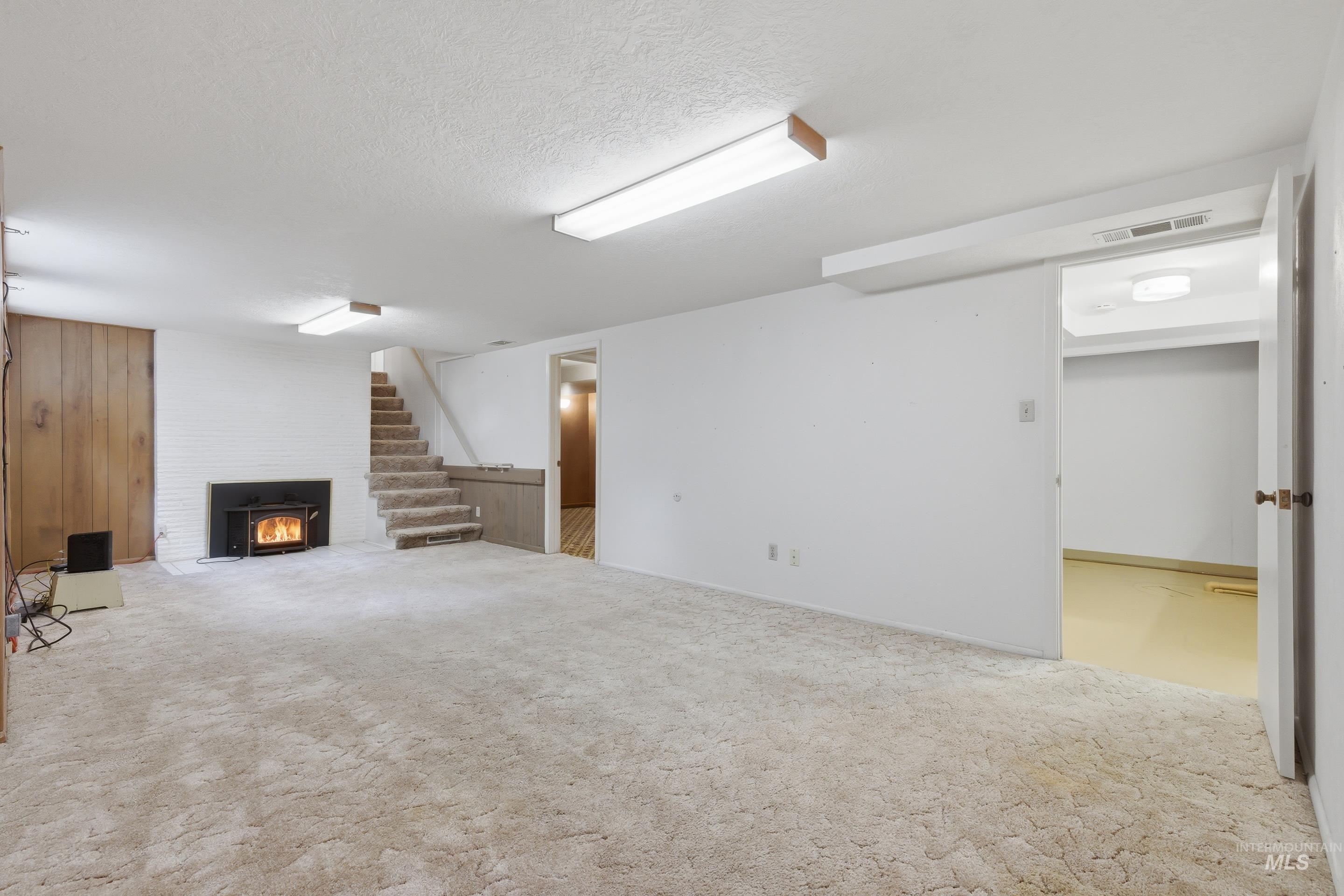 504 West Howe Street Boise, ID 83706 - Photo 38 of 47 Spacious finished basement featuring a wood-burning fireplace insert with a painted brick surround, wood paneling accent wall, recessed lighting, and carpet flooring