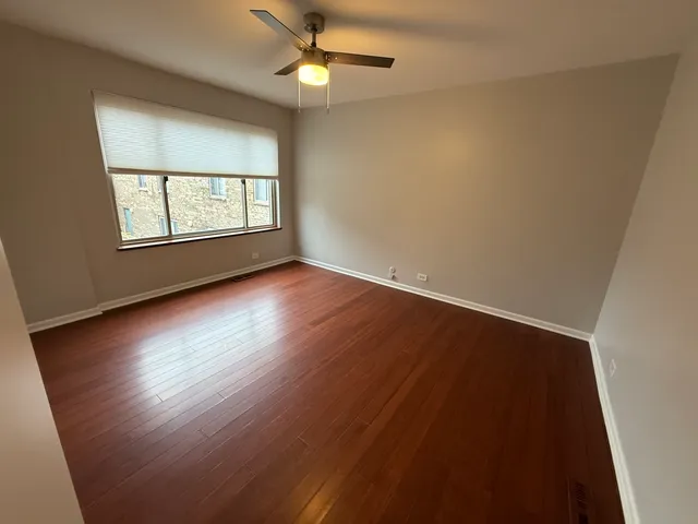 an empty room with wooden floor chandelier fan and windows