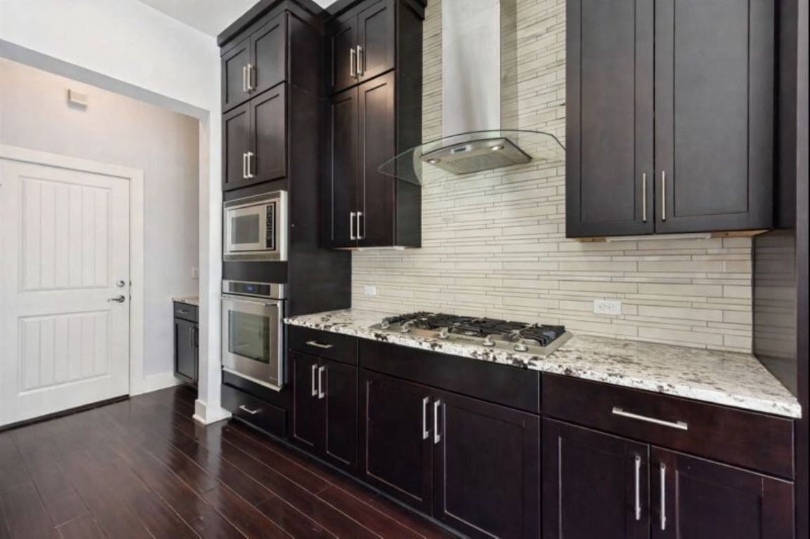 8110 Ranch Road 2222, Unit 98 Austin, TX 78730 - Photo 9 of 37 Kitchen featuring wall chimney exhaust hood, stainless steel appliances, light stone countertops, and dark wood-style floors