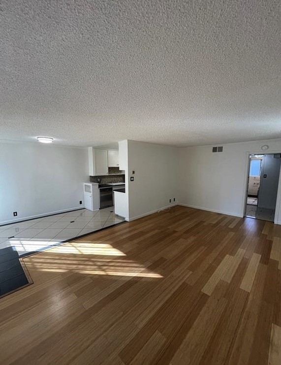 a view of empty room with wooden floor and kitchen
