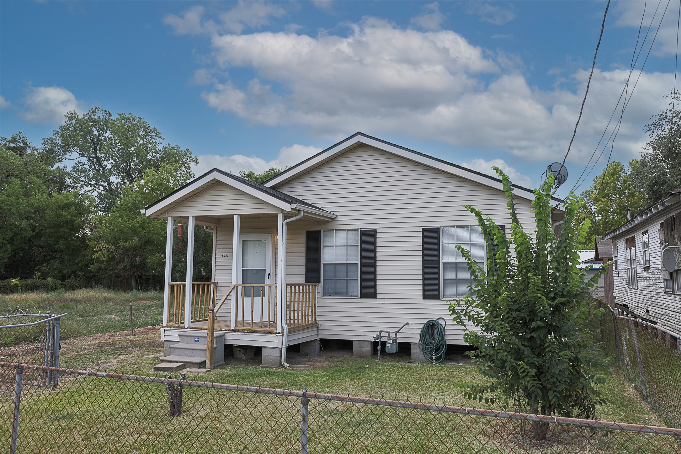This is a modest single-story home featuring a small front porch, beige siding, and shutters. 