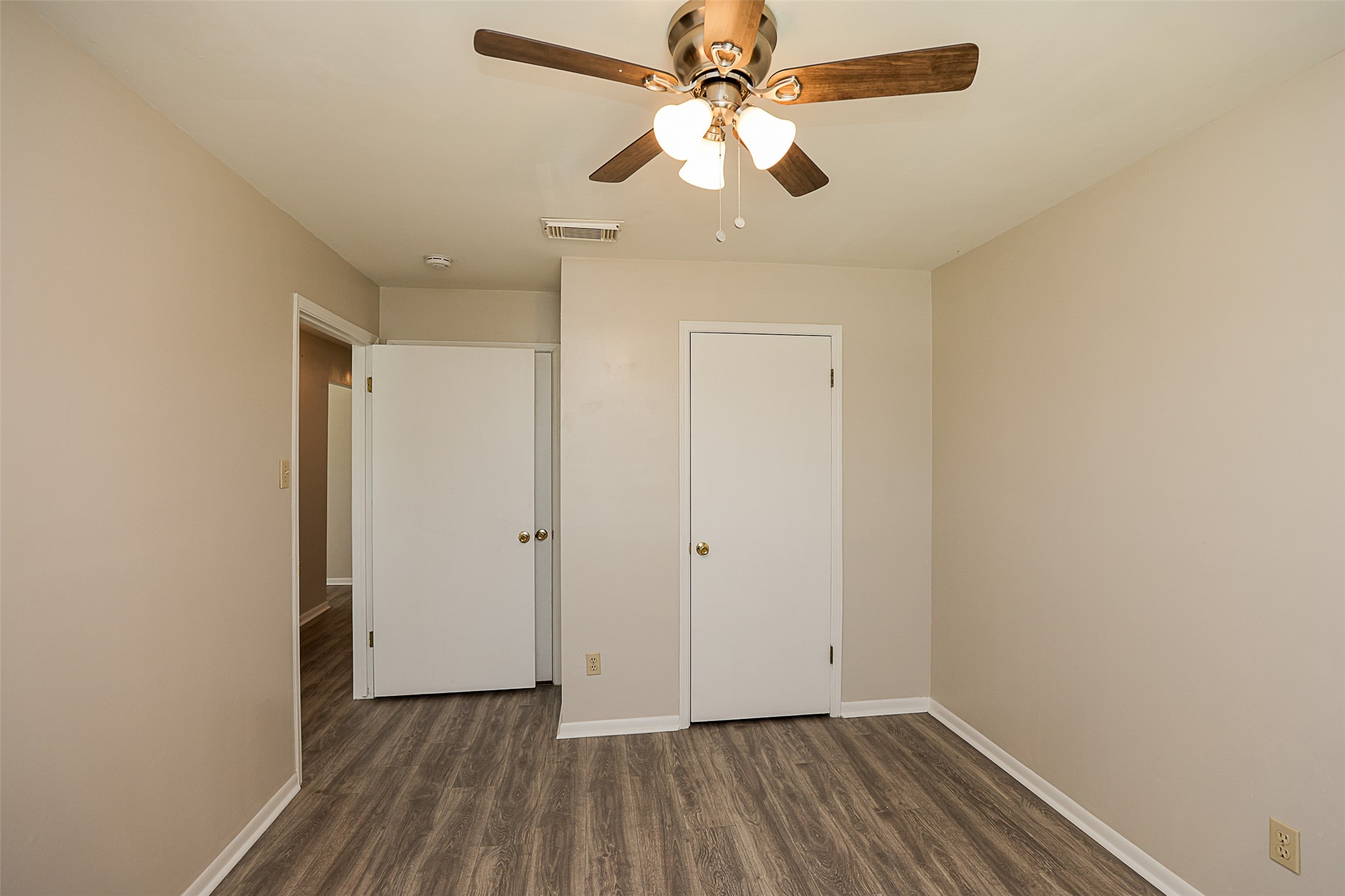 7810 Queen Street Houston, TX 77028 - Photo 12 of 21 This is a well-lit, primary bedroom featuring a ceiling fan with lights, wood-look laminate flooring, a closet and entry to the bathroom.