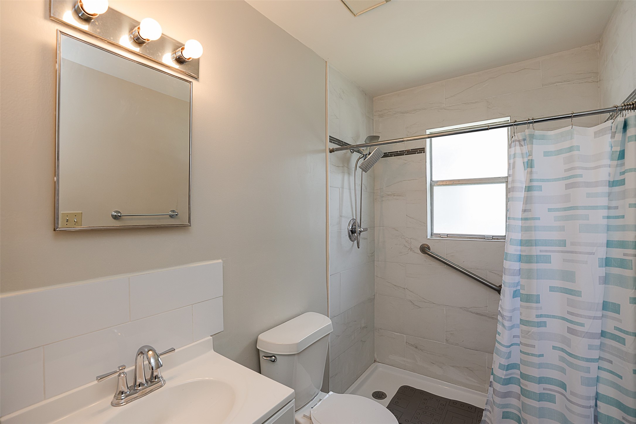 7810 Queen Street Houston, TX 77028 - Photo 13 of 21 A clean, well-lit bathroom with a shower, tiled walls, a vanity with a sink and mirror, and a frosted window for natural light and privacy.
