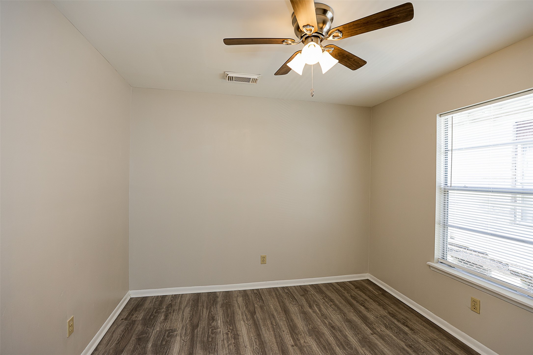 7810 Queen Street Houston, TX 77028 - Photo 14 of 21 This is a well-lit, second bedroom featuring neutral walls, wood-look flooring, and a ceiling fan with lights.