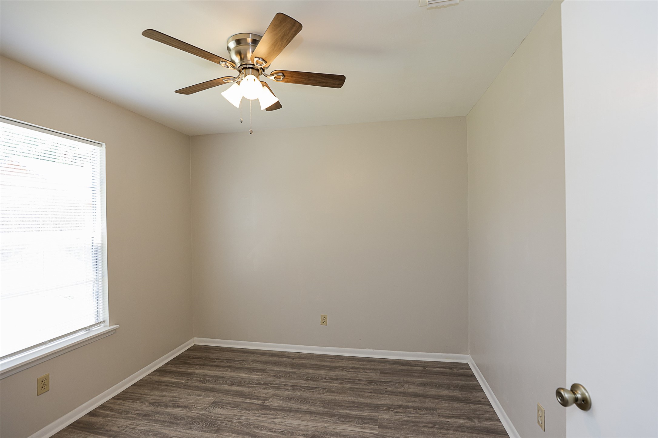 7810 Queen Street Houston, TX 77028 - Photo 16 of 21 This is a well-lit, third bedroom featuring a ceiling fan with a light fixture, laminate wood flooring, and a window with blinds.