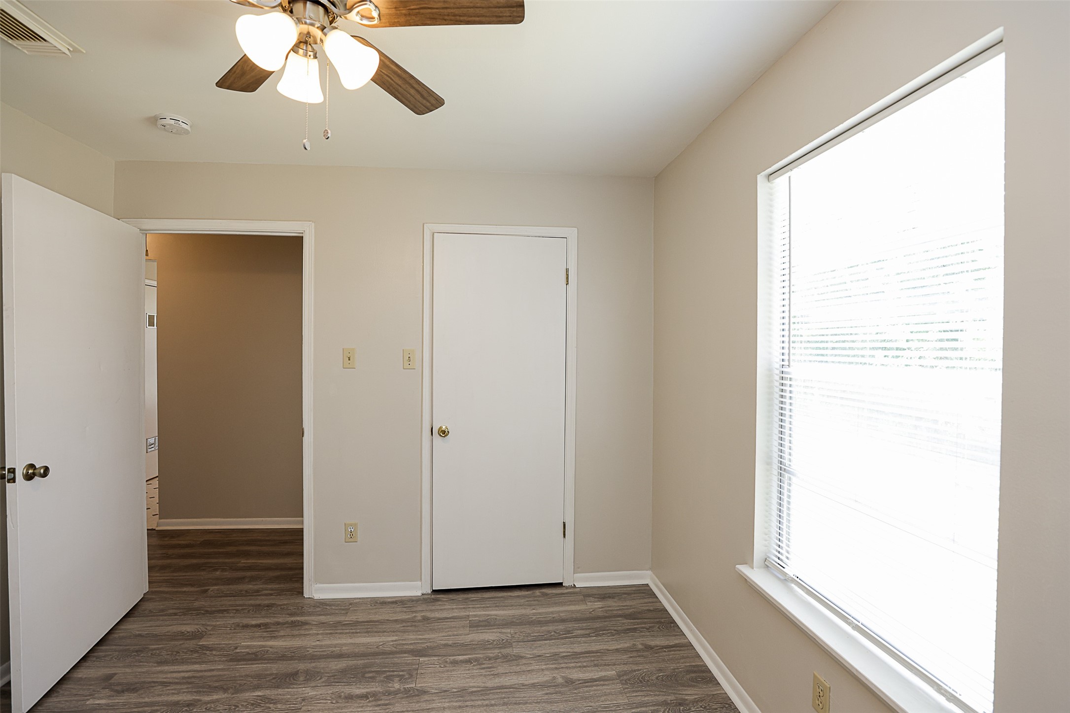 7810 Queen Street Houston, TX 77028 - Photo 17 of 21 This is a bright, third bedroom with modern wood-look flooring, neutral walls, a ceiling fan with lighting, and a large window allowing for natural light. The room features two doors, one leading to a closet and the other to the hallway.