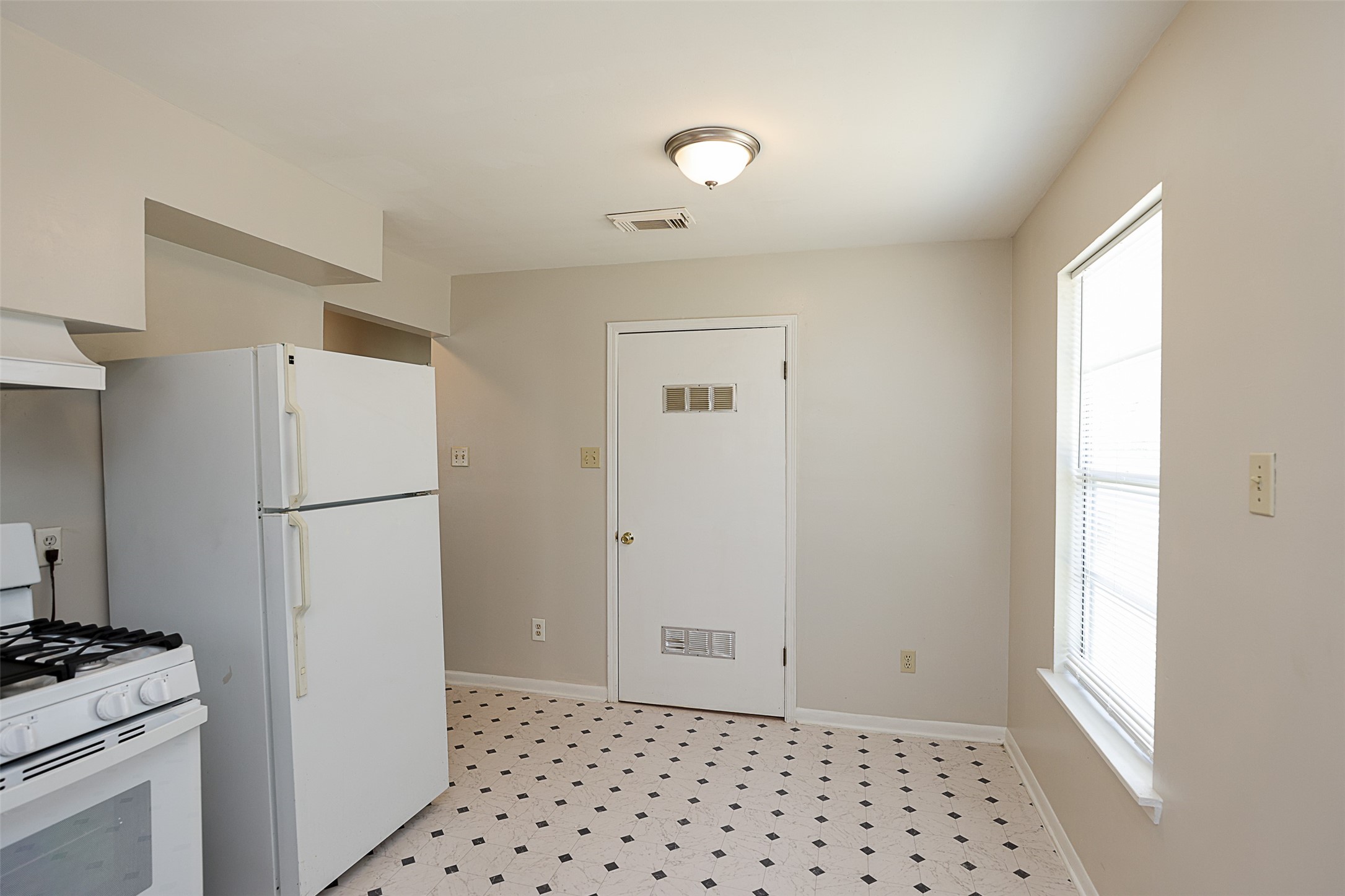 7810 Queen Street Houston, TX 77028 - Photo 9 of 21 This is a modest-sized kitchen with basic white appliances, including a refrigerator and a gas stove. It features a neutral color palette, vinyl tile flooring with a diamond pattern, and a window providing natural light.