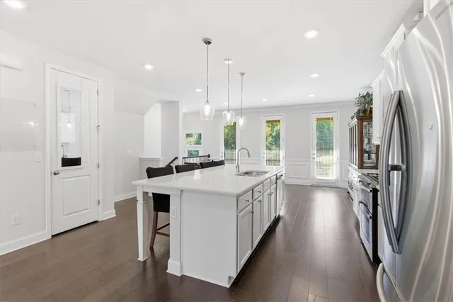 a kitchen with stainless steel appliances granite countertop a refrigerator a sink dishwasher a stove and a dining table with wooden floor