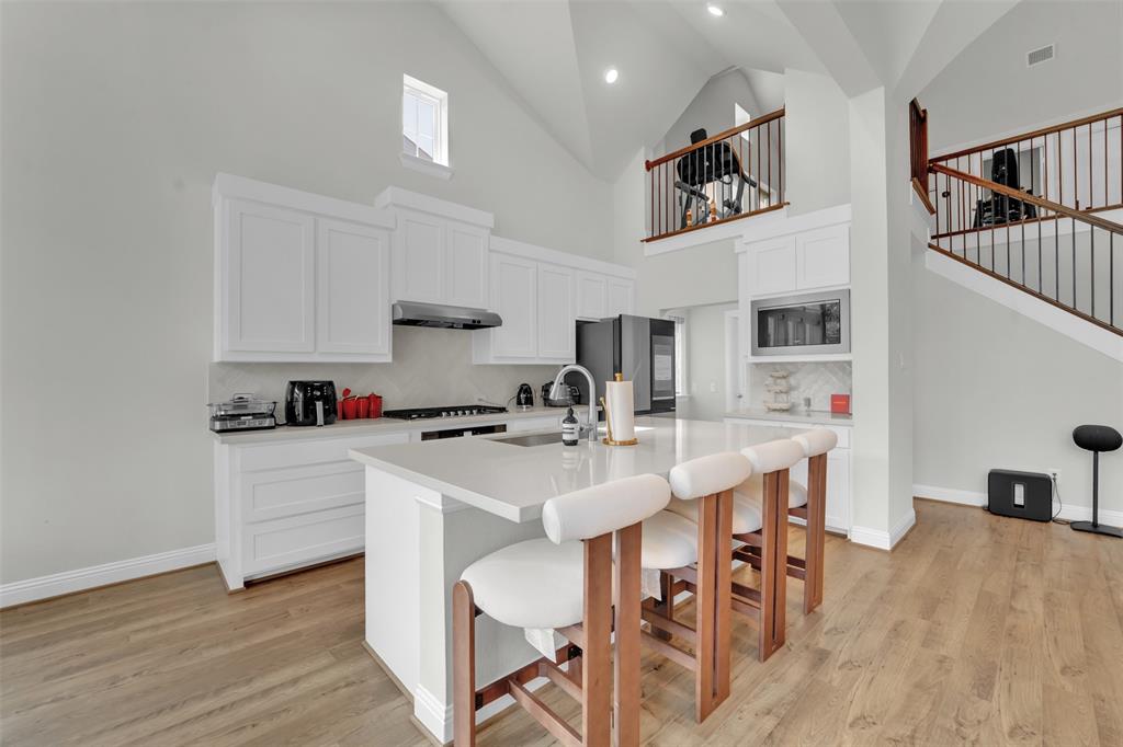 3520 Helios Lane Corinth, TX 76208 - Photo 10 of 37 Modern kitchen featuring an island with seating, white shaker-style cabinetry, light-toned wood-finish flooring, and a second-story interior balcony