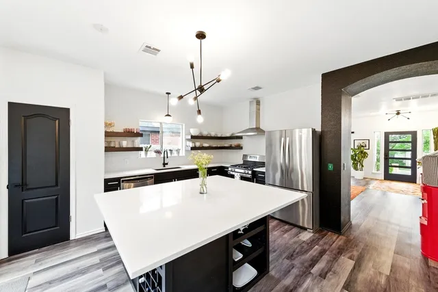 a kitchen with stainless steel appliances a refrigerator a sink dishwasher a stove and a dining table with wooden floor