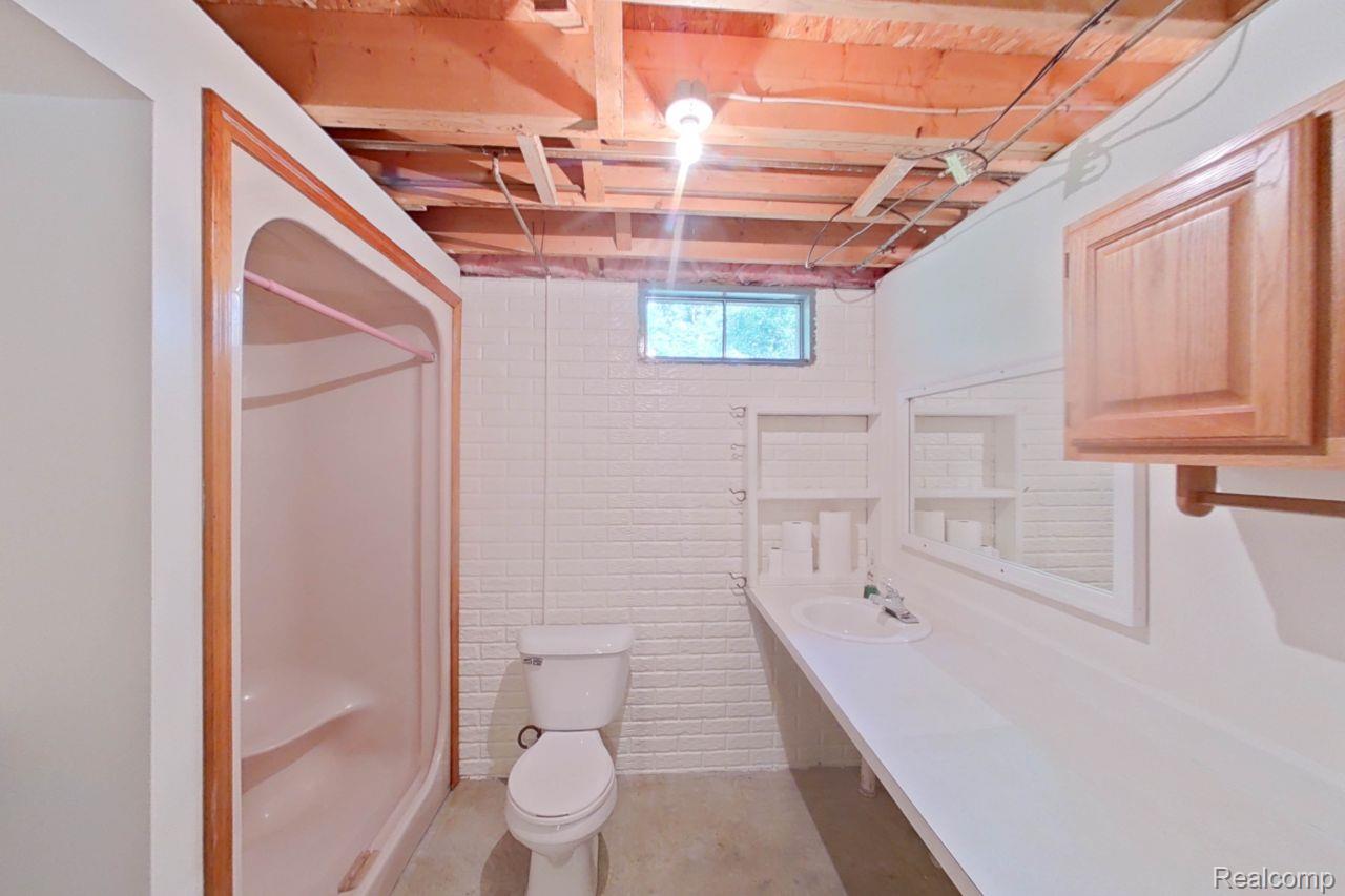 10201 Washburn Road Goodrich, MI 48438 - Photo 61 of 85 Bathroom featuring an exposed wood joist ceiling, an integrated shower, a white toilet, an elongated vanity with an integrated sink, and an overhead light fixture