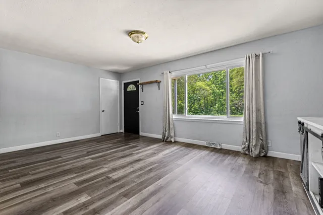 a view of an empty room with wooden floor and a window