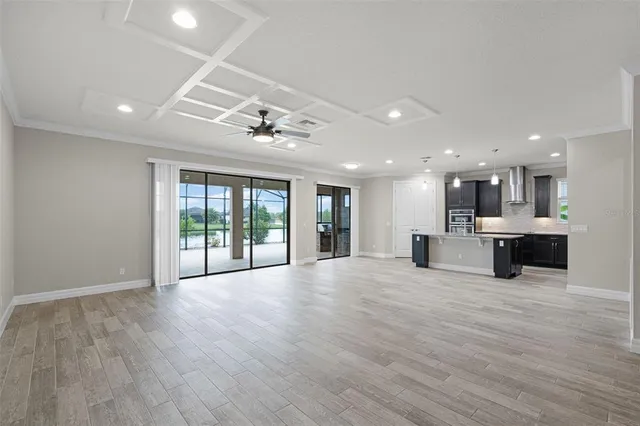 a view of an empty room with wooden floor and a kitchen