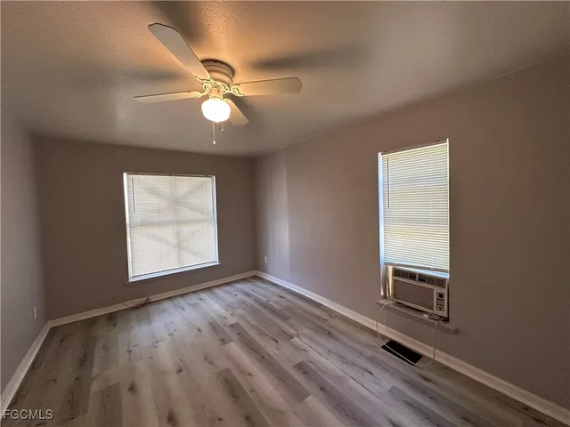 an empty room with wooden floor fan and windows