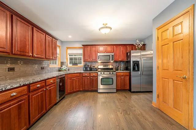 a kitchen with stainless steel appliances granite countertop a refrigerator a sink dishwasher a stove and wooden cabinets with wooden floor