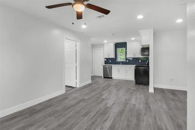 an empty room with wooden floor a ceiling fan and kitchen view
