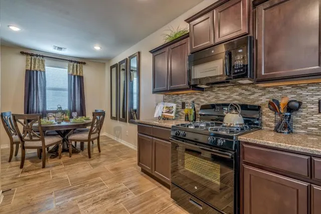 a kitchen with stainless steel appliances granite countertop a stove top oven a sink dishwasher a dining table and chairs with wooden floor