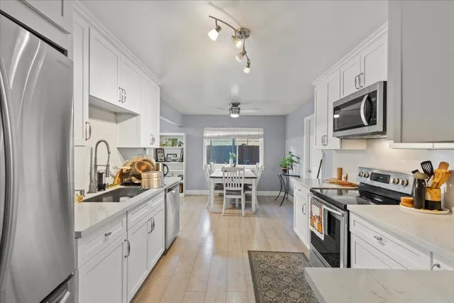 a kitchen with stainless steel appliances a stove a sink dishwasher a refrigerator and a dining table with wooden floor