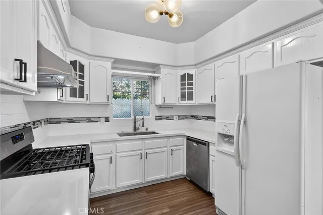 a kitchen with a sink dishwasher a stove a refrigerator and white cabinets with wooden floor