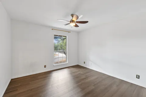 an empty room with wooden floor ceiling fan and windows