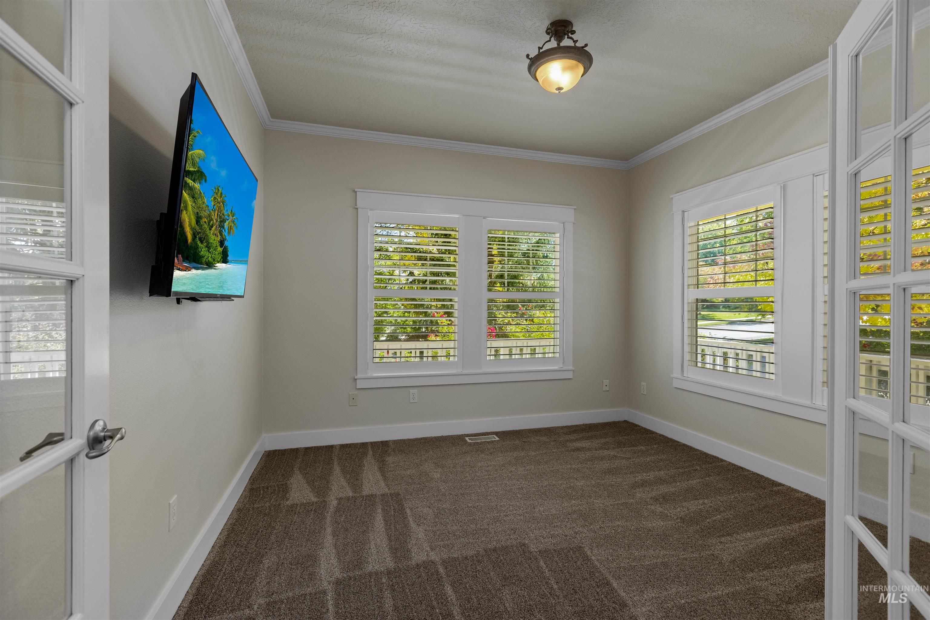 5426 West School Ridge Road Boise, ID 83714 - Photo 13 of 39 Double French doors with glass panes, crown molding, two windows with plantation shutters, patterned carpet, and a flush mount light fixture