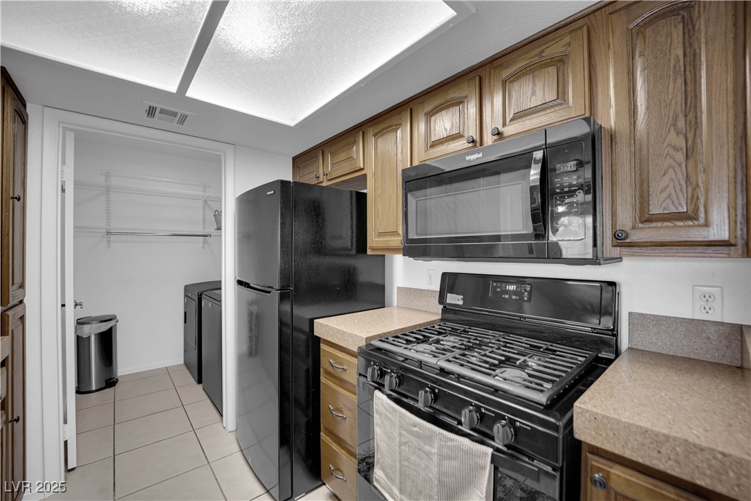 1909 Mountain Hills Court, Unit 205 Las Vegas, NV 89128 - Photo 15 of 34 Kitchen featuring black appliances, light countertops, light tile patterned floors, a textured ceiling, and brown cabinets