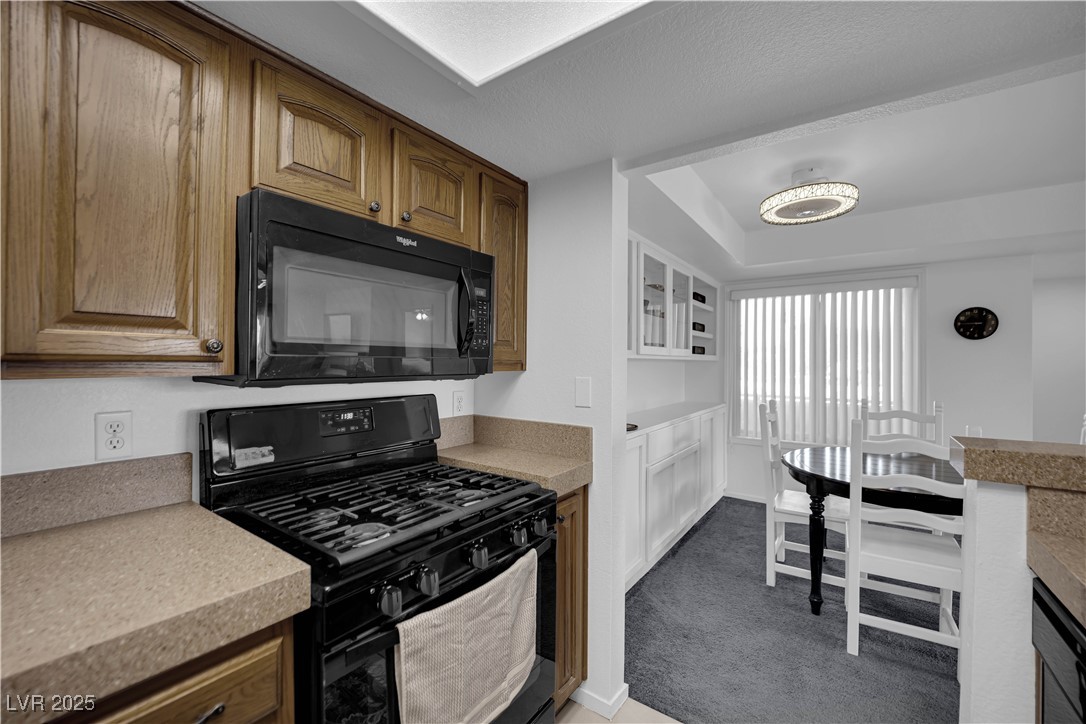 1909 Mountain Hills Court, Unit 205 Las Vegas, NV 89128 - Photo 17 of 34 Kitchen featuring black appliances, brown cabinetry, dark carpet, a textured ceiling, and glass insert cabinets