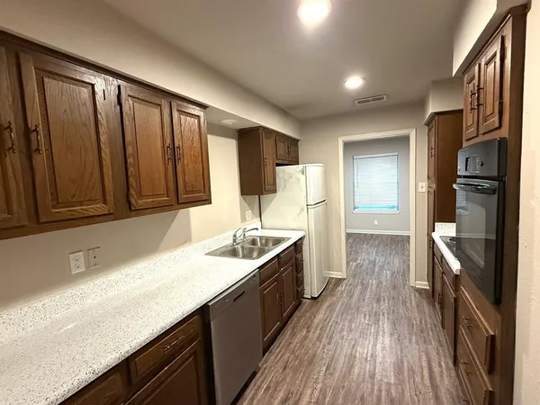a kitchen with stainless steel appliances granite countertop a refrigerator a sink dishwasher a stove and white countertops with wooden floor
