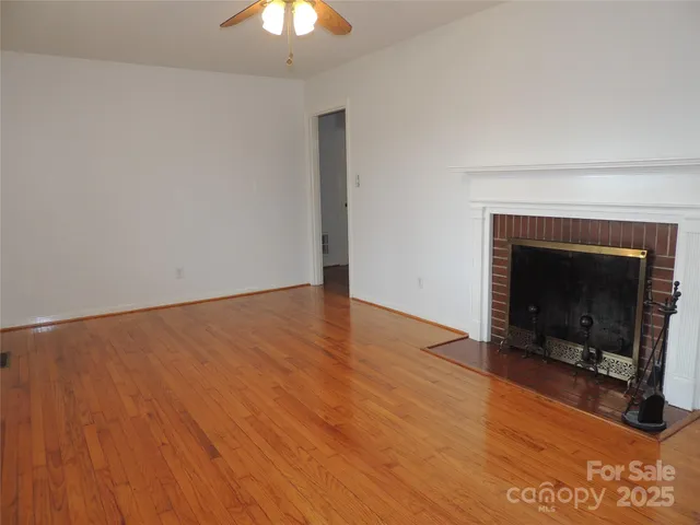 a view of an empty room with wooden floor fireplace and a window