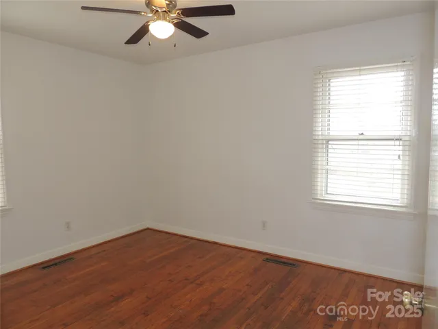 an empty room with wooden floor chandelier fan and windows