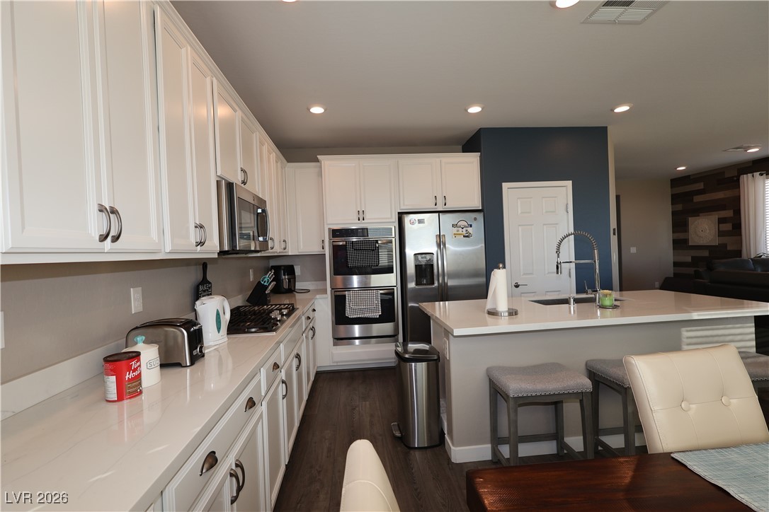 764 Rogue Wave Street Las Vegas, NV 89138 - Photo 22 of 36 Kitchen featuring light stone counters, a breakfast bar, stainless steel appliances, an island with sink, and white cabinetry