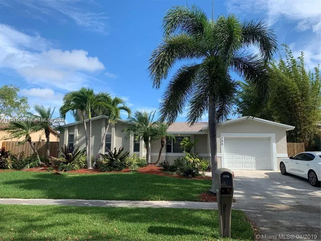 a view of a white house with a yard and palm trees