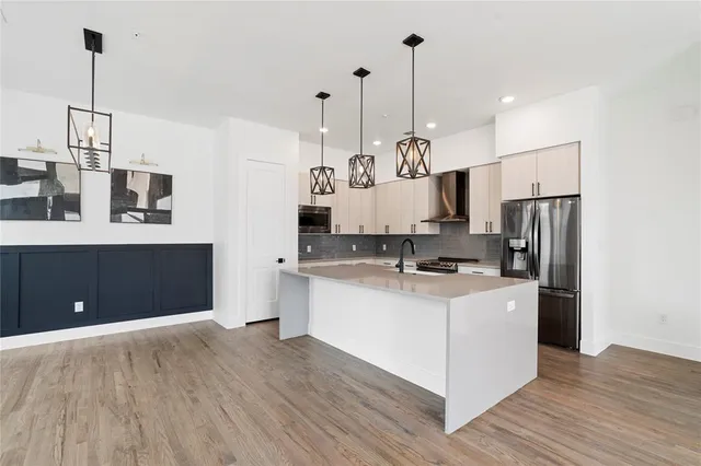 a kitchen with stainless steel appliances granite countertop a sink a stove a refrigerator and white cabinets with wooden floor