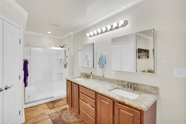 a bathroom with a granite countertop double vanity sink a mirror and shower
