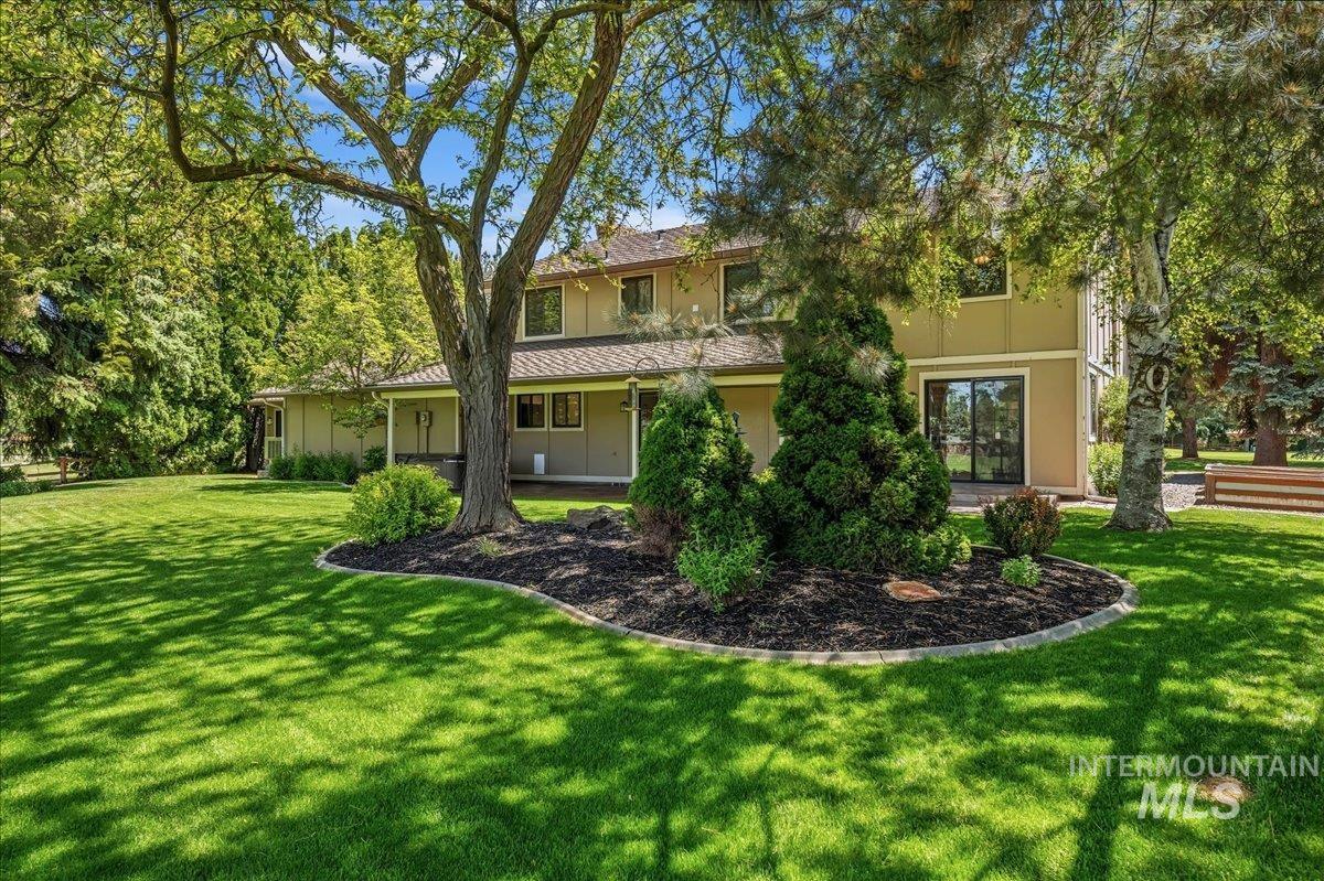 599 Pebble Beach Way Eagle, ID 83616 - Photo 34 of 44 Expansive manicured lawn with mature shade trees, established landscaping, and a two-story exterior featuring a covered patio and sliding glass door access