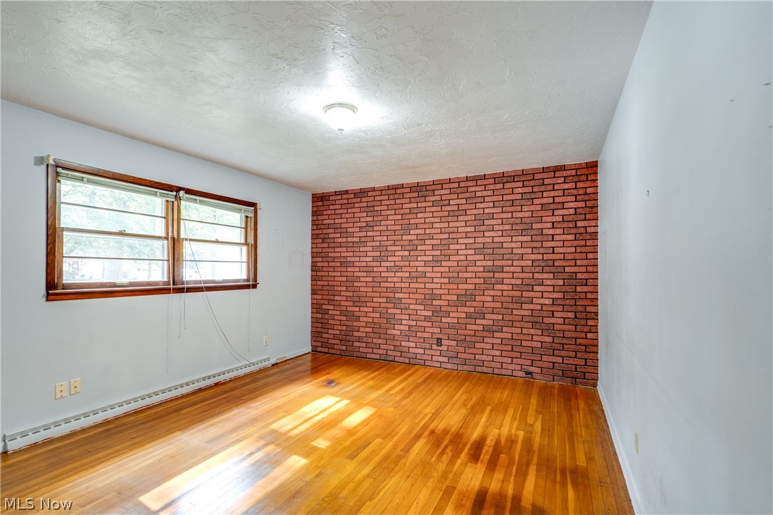 3799 Boydell Road Kent, OH 44240 - Photo 8 of 21 Empty room featuring brick wall, light wood-type flooring, a baseboard heating unit, and a textured ceiling