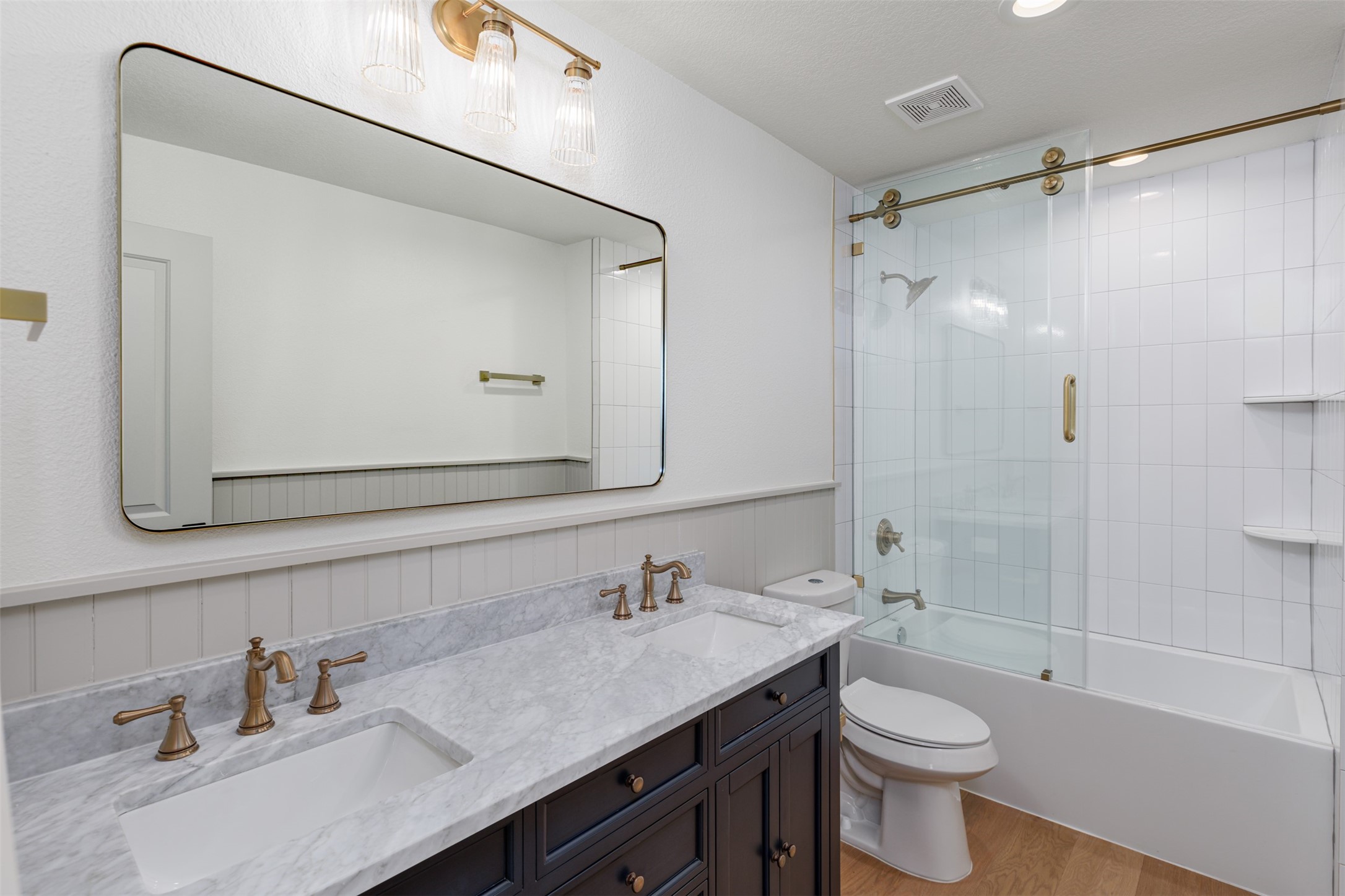 1535 Rutland Street Houston, TX 77008 - Photo 33 of 46 Bathroom with double vanities, tub shower combination with fully textured tiled ceramic wall to tub surround behind a glass sliding double door for easy access. Glass wall mounted access lighting and champagne vintage brass hardware continue the design them. The accent bead board adds additional design detail reflective of the original era of the home.
