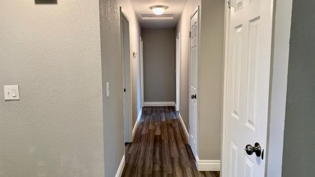 a view of a hallway with wooden floor and a bathroom