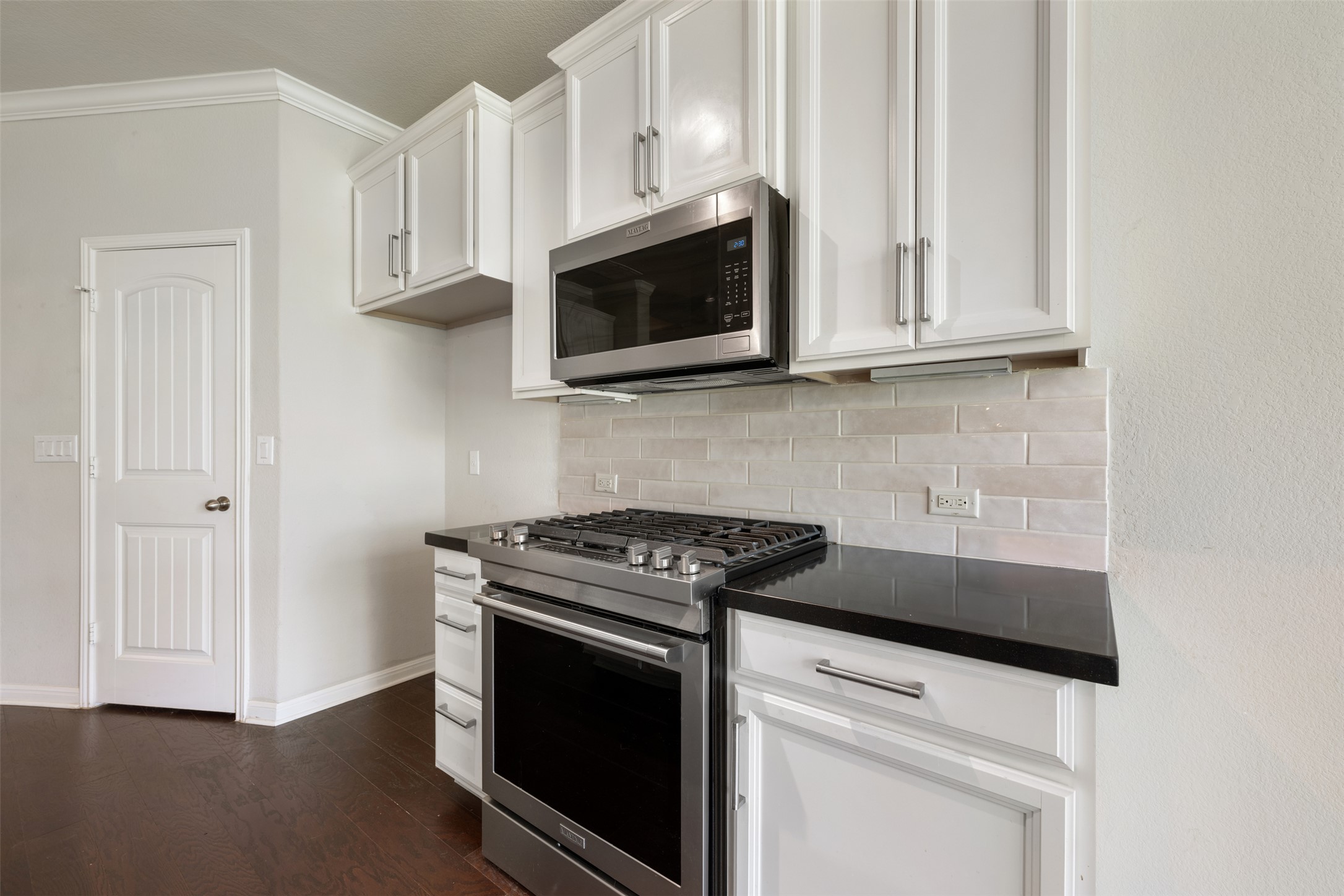 211 Parable Cove Pflugerville, TX 78660 - Photo 12 of 40 Kitchen featuring stainless steel range with gas cooktop, microwave, white cabinetry, dark countertops, and subway tile backsplash