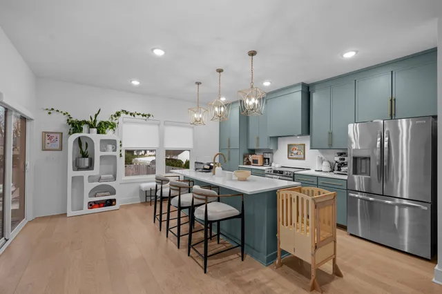 a kitchen with stainless steel appliances a refrigerator a stove a sink dishwasher a dining table and chairs with wooden floor