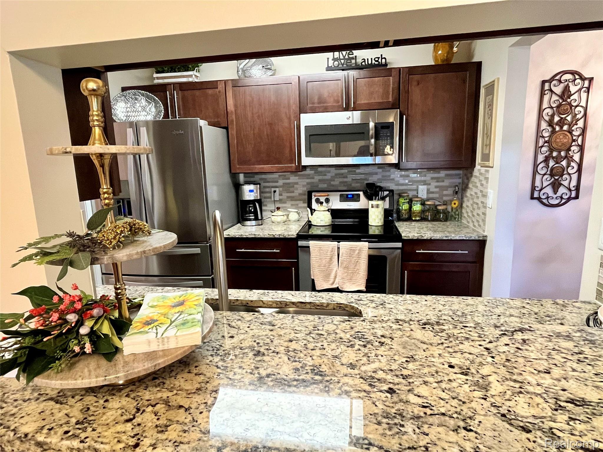 3624 Oakmonte Boulevard, Unit 82 Rochester, MI 48306 - Photo 5 of 37 Kitchen with stainless steel appliances, dark wood finish cabinets, light stone counters, and backsplash