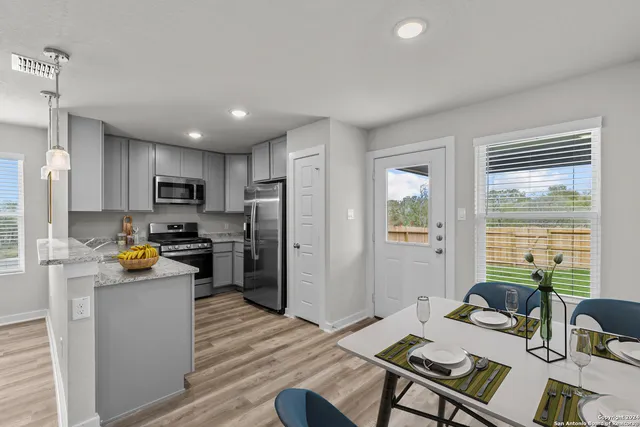 a open kitchen with stainless steel appliances granite countertop a refrigerator a stove top oven a sink dishwasher a dining table and chairs with wooden floor