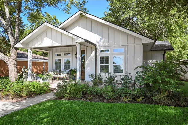 a view of a white house next to a yard with plants and trees