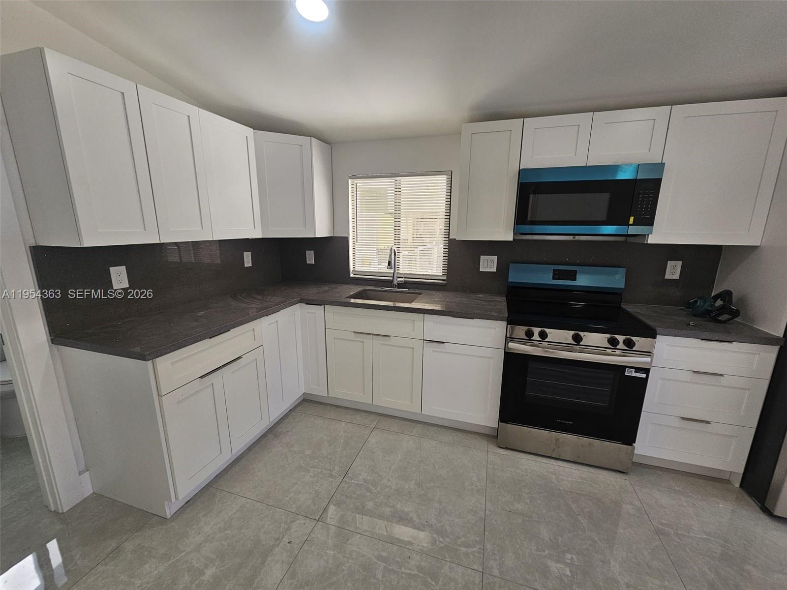1148 Northwest 100th Street, Unit 1 Miami, FL 33150 - Photo 19 of 32 a white kitchen with granite countertop a sink a stove a microwave a refrigerator and cabinets