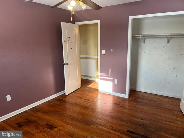a view of an empty room with wooden floor and a ceiling fan