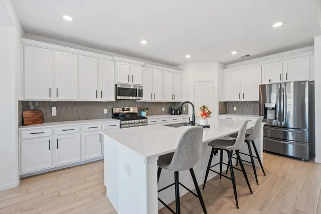 a kitchen with stainless steel appliances granite countertop a stove a sink a microwave a refrigerator and white cabinets with wooden floor