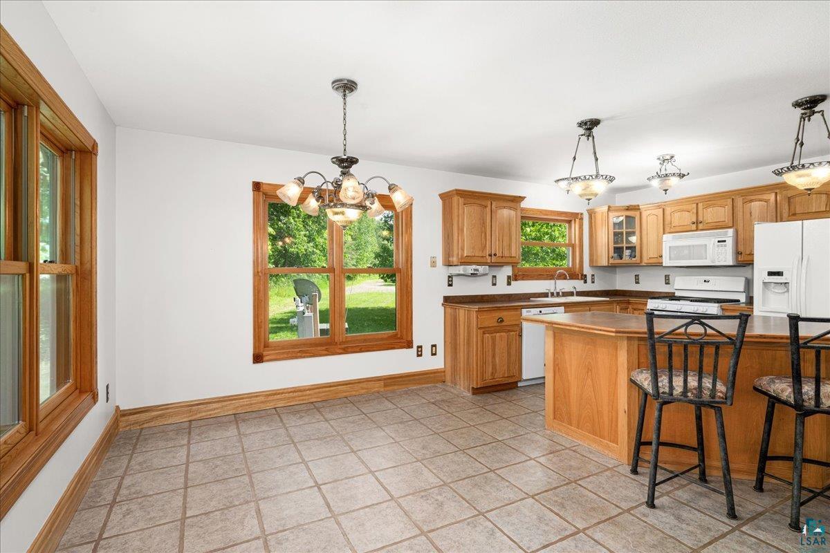 3799 South Lake Road Moose Lake, MN 55767 - Photo 8 of 35 Kitchen and dining area featuring tile flooring, light wood cabinetry, white appliances, and multiple windows with wood trim