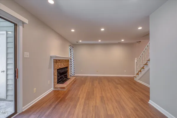 an empty room with wooden floor fireplace and windows